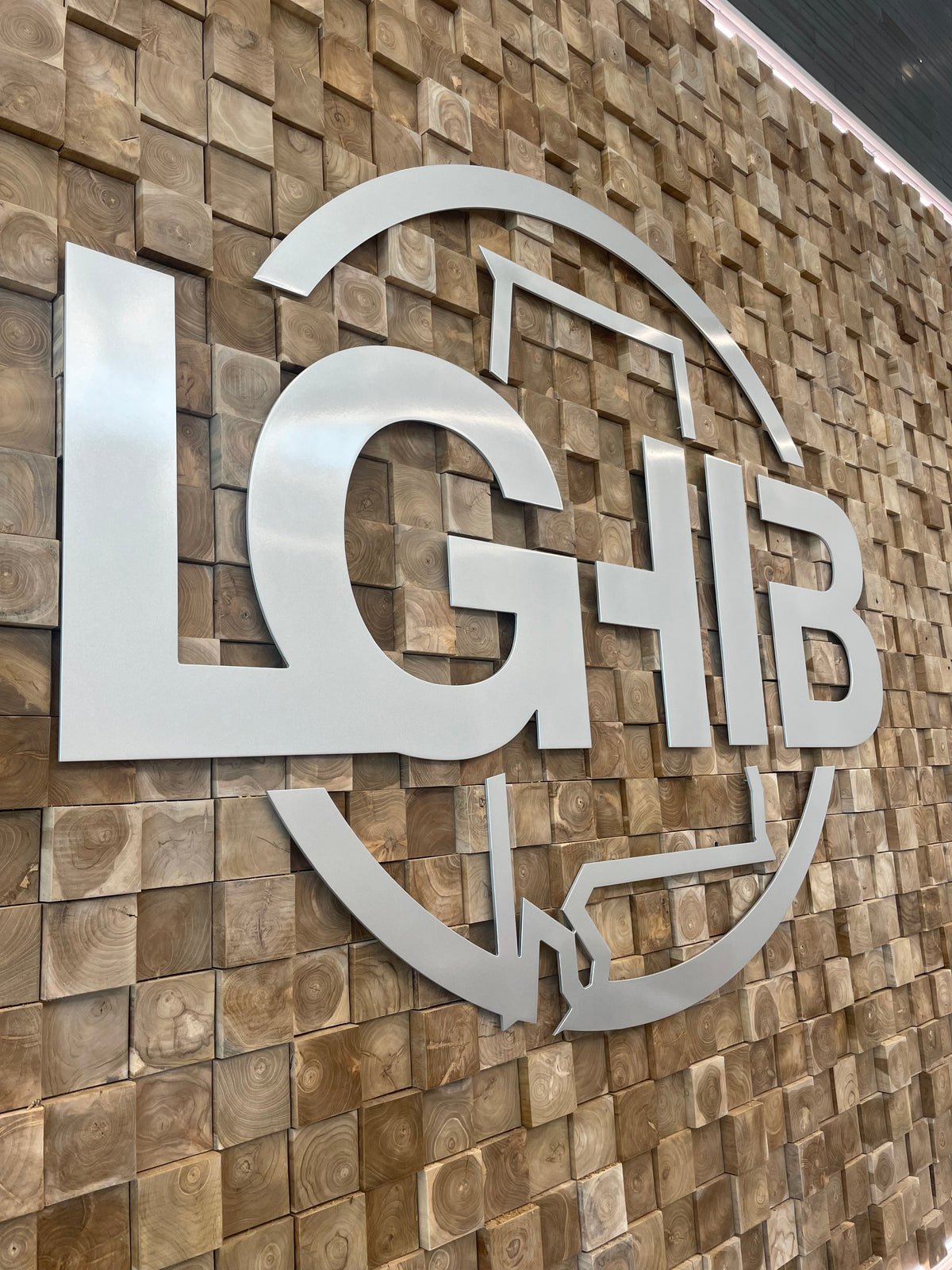 Large dimensional LGHIB logo fabricated in brushed silver and mounted on a decorative wood block feature wall.